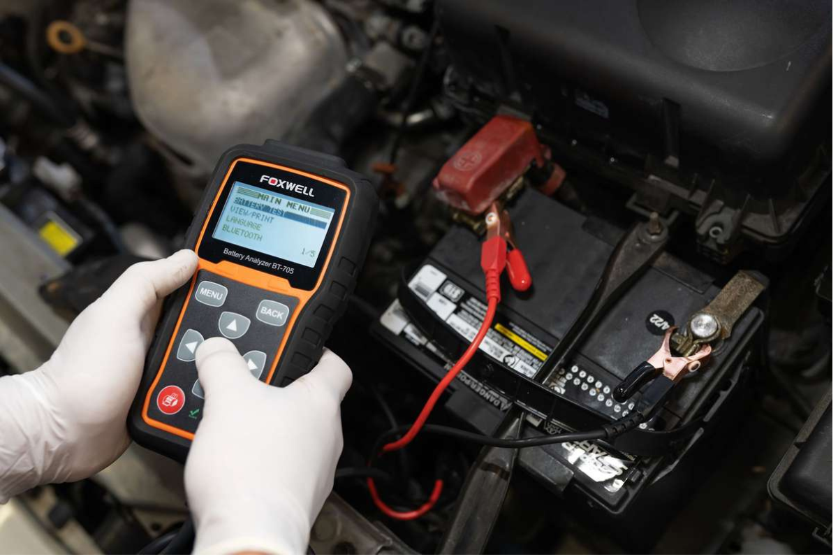 battery replacement service in boca raton, fl by boca auto fix. image showing a technician testing a car battery using a foxwell battery analyzer, highlighting the importance of accurate diagnostics and professional battery replacement services for reliable vehicle performance.