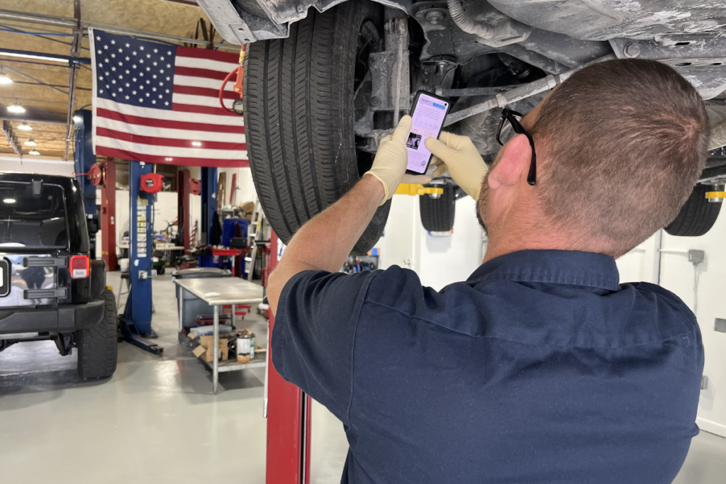 technician performing a digital vehicle inspection (dvi) on a car in boca raton, fl. the image shows the technician under the car with a phone, capturing detailed photos and videos of the vehicle's condition for a comprehensive and transparent inspection report at boca auto fix.