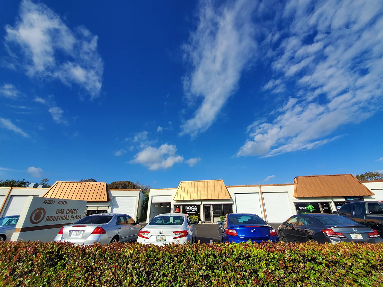 a row of honda vehicles parked in front of businesses at boca auto. the sky is clear with scattered clouds.