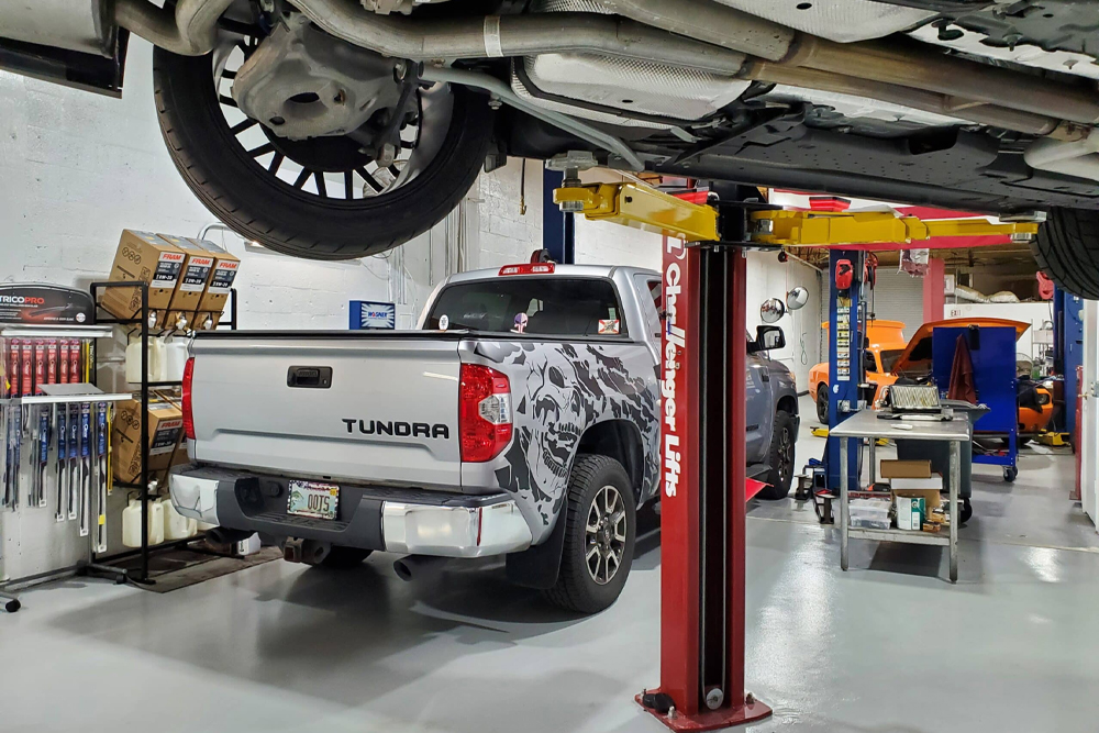 automotive repair shop with a white toyota tundra under a red auto lift, surrounding shelves with automotive supplies.