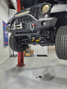 how car fluid leaks impact your safety and cars performance in boca raton, fl. with boca auto fix. image of red sedan on lift in the shop with red fluid leaked on the floor due to a power steering fluid leak.