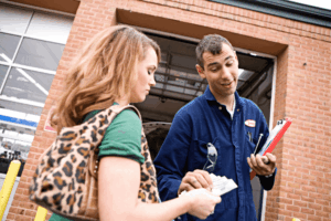 Auto mechanic in Boca Raton, FL by Boca Auto Fix. Image of a technician receiving payment from a customer outside of an auto repair shop.