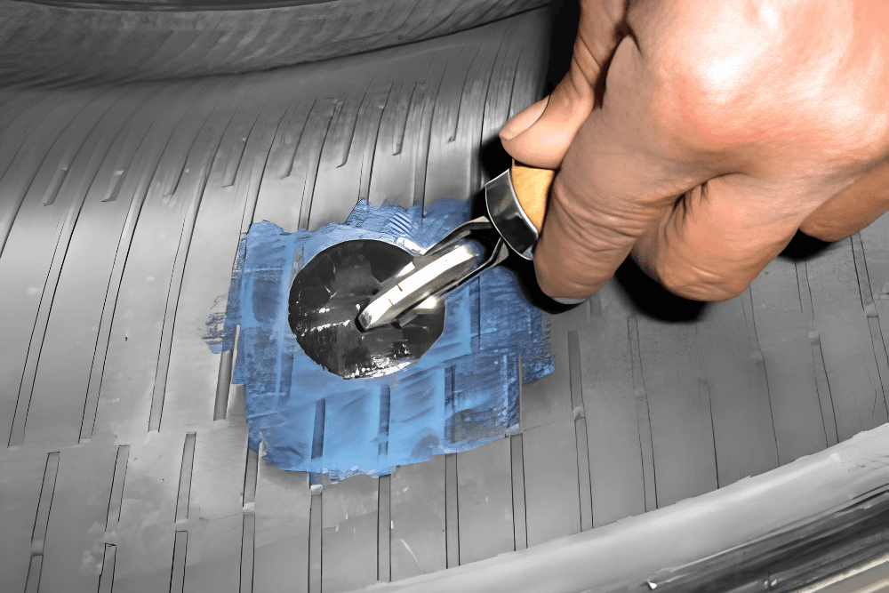 Tire Repair in Boca Raton, FL at Boca Auto Fix. An image of a hand uses a wooden-handled tire repair tool to pull the metal stem of a patch-plug through a blue and black patch on the tire's inner lining.