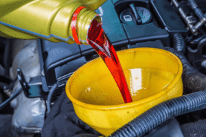 transmission fluid service, auto repair in boca raton, fl at boca auto fix. image of red transmission fluid being poured through a yellow funnel into a vehicle engine bay during maintenance.